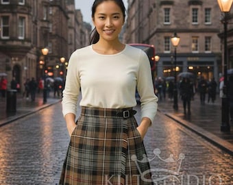 May include: A woman wearing a cream-colored long-sleeve shirt and a plaid skirt with a black belt. The skirt features a brown, gray, and black tartan pattern. The image includes the text "KILT STUDIO KILTS & ACCESSORIES".