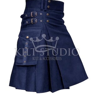 Op de afbeelding: Een marineblauwe kilt met plooien, een zak en decoratieve gespen. De kilt heeft de tekst "Kilt Studio Kilt & Accessories". De kilt heeft messingkleurige knopen en klinknagels.