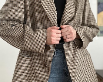 May include: A brown and black houndstooth blazer with a classic notched lapel. The blazer has two buttons and is worn over a black turtleneck and blue jeans. The blazer is a stylish piece of outerwear.