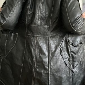 May include: Black leather jacket with white stitching details. The jacket features multiple pockets and a classic design. The leather appears worn, adding character to the garment. A stylish outerwear piece.