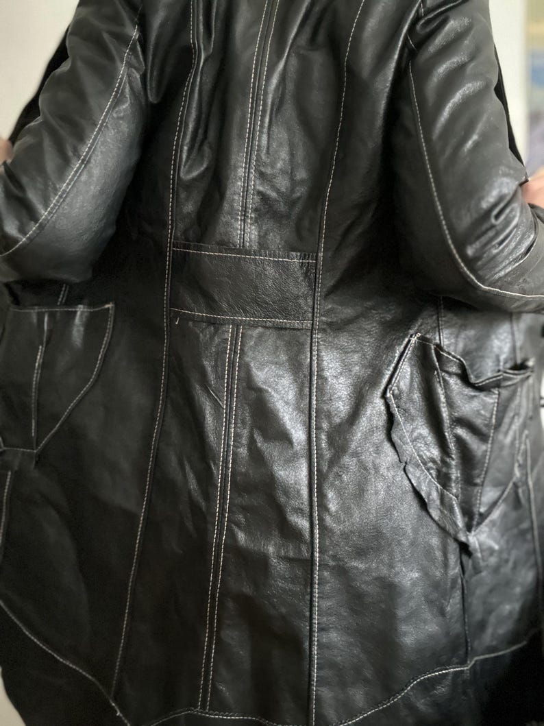 May include: Black leather jacket with white stitching details. The jacket features multiple pockets and a classic design. The leather appears worn, adding character to the garment. A stylish outerwear piece.