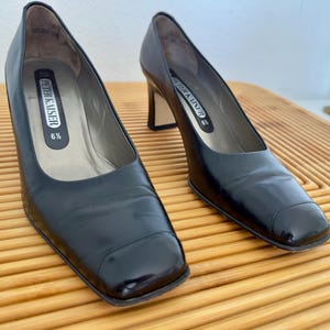 Puede incluir: Un par de zapatos de tacón Peter Kaiser de cuero negro. Los zapatos tienen punta cuadrada, tacón medio y el nombre de la marca es visible en la plantilla. Talla 37.