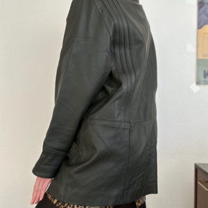 May include: A dark green leather jacket with a collared neckline and vertical stitched details on the upper back. The jacket has a tailored fit and a classic design, suitable for various occasions.