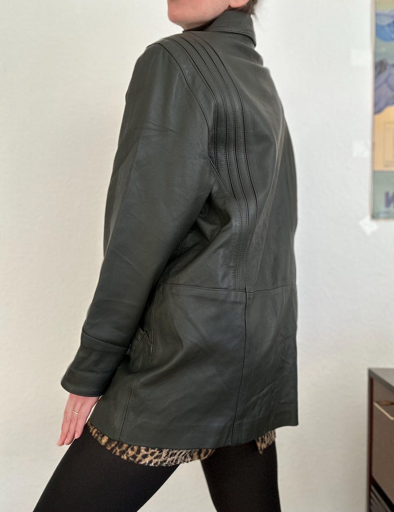 May include: A dark green leather jacket with a collared neckline and vertical stitched details on the upper back. The jacket has a tailored fit and a classic design, suitable for various occasions.
