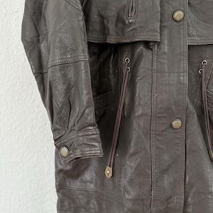 Puede incluir: Chaqueta de cuero marr&oacute;n con cierre de botones, cuello alto y m&uacute;ltiples bolsillos. La chaqueta tiene un dise&ntilde;o cl&aacute;sico con un corte entallado, y las mangas tienen pu&ntilde;os abotonados. Hecha de cuero suave y flexible.