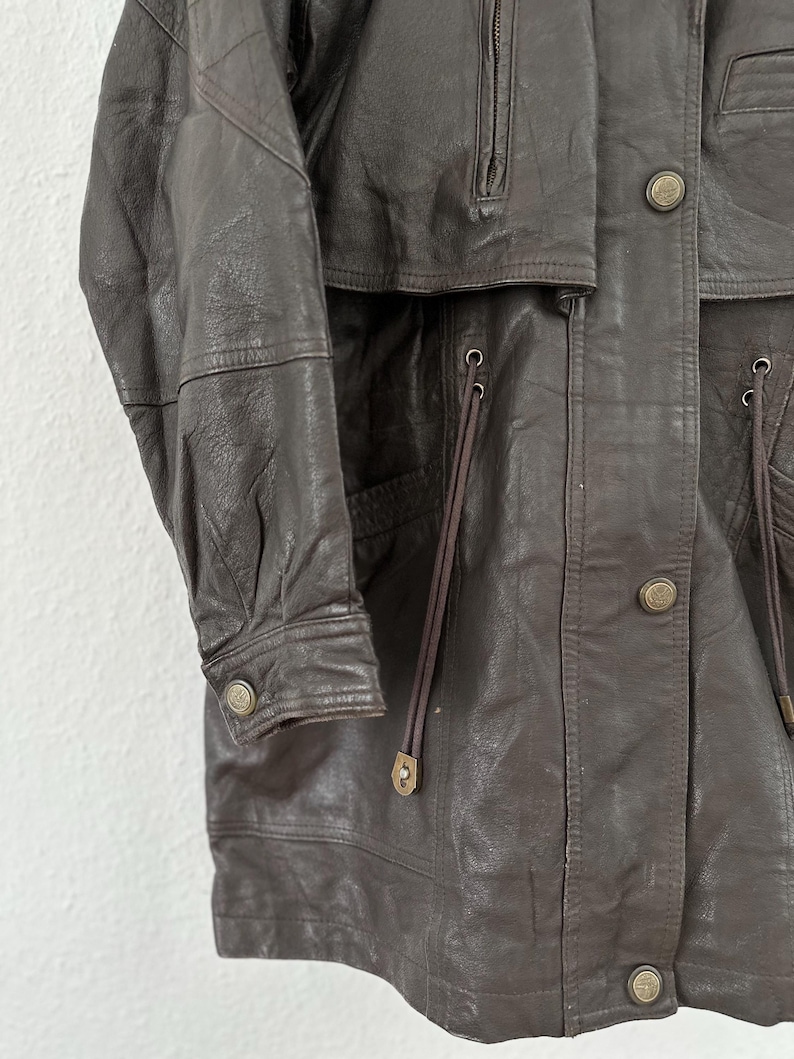 Puede incluir: Chaqueta de cuero marr&oacute;n con cierre de botones, cuello alto y m&uacute;ltiples bolsillos. La chaqueta tiene un dise&ntilde;o cl&aacute;sico con un corte entallado, y las mangas tienen pu&ntilde;os abotonados. Hecha de cuero suave y flexible.