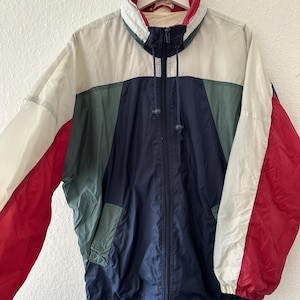Può includere: Giacca a vento vintage a blocchi di colore rosso, bianco, blu navy e verde. La giacca ha un collo alto, una cerniera a tutta lunghezza e un cordino sull'orlo. Le maniche sono lunghe e la giacca è appesa a una gruccia bianca.