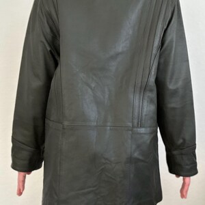 May include: A dark green leather jacket with a collared neckline and long sleeves. The back of the jacket features vertical stitched detailing on the shoulders. The jacket is knee-length and has a leopard print hem.
