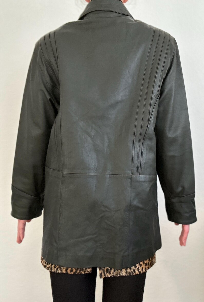 May include: A dark green leather jacket with a collared neckline and long sleeves. The back of the jacket features vertical stitched detailing on the shoulders. The jacket is knee-length and has a leopard print hem.