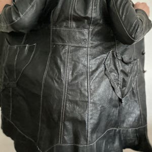 May include: Black leather coat with white stitching details. The coat features a classic design with a notched collar, pockets, and a flared hem. The stitching adds a contrasting element to the coat's sleek appearance. A stylish outerwear piece.