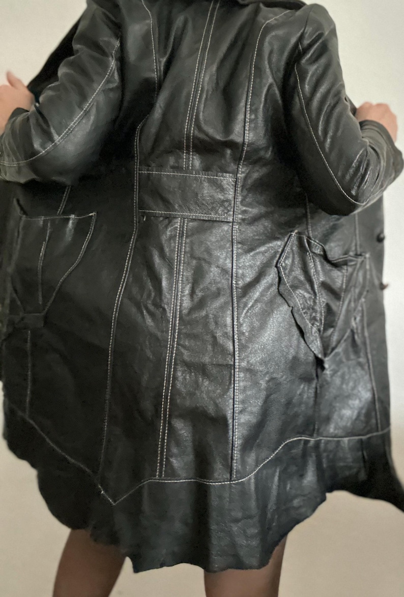 May include: Black leather coat with white stitching details. The coat features a classic design with a notched collar, pockets, and a flared hem. The stitching adds a contrasting element to the coat's sleek appearance. A stylish outerwear piece.