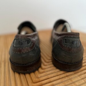 Puede incluir: Un par de mocasines de cuero marr&oacute;n oscuro con tal&oacute;n y ribete marr&oacute;n oscuro en contraste. Los zapatos tienen un dise&ntilde;o cl&aacute;sico, adecuado para uso informal o semiformal. Las suelas tambi&eacute;n son de color marr&oacute;n oscuro.
