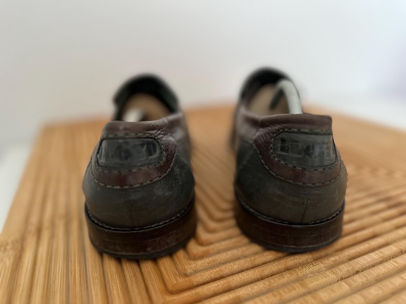 Puede incluir: Un par de mocasines de cuero marr&oacute;n oscuro con tal&oacute;n y ribete marr&oacute;n oscuro en contraste. Los zapatos tienen un dise&ntilde;o cl&aacute;sico, adecuado para uso informal o semiformal. Las suelas tambi&eacute;n son de color marr&oacute;n oscuro.