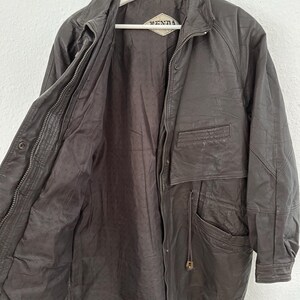 Puede incluir: Chaqueta de cuero marr&oacute;n oscuro con cierre de cremallera y m&uacute;ltiples bolsillos. La chaqueta est&aacute; colgada de una percha blanca. El forro interior es de un tono marr&oacute;n m&aacute;s oscuro. La chaqueta tiene la marca "DENNA" en una etiqueta.