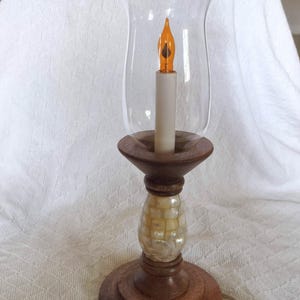 Puede incluir: Lámpara de vela eléctrica decorativa con pantalla de vidrio transparente. La lámpara tiene una base de madera y un tallo decorativo con diseño de nácar. La vela tiene una llama naranja.