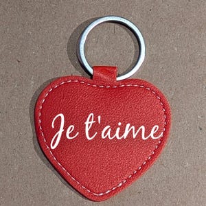 Peut inclure: Un porte-clés rouge en forme de cœur avec l'inscription "Je t'aime" en écriture blanche. Le porte-clés est doté d'un anneau en métal argenté et d'une bordure cousue. Le cœur est en matière texturée.