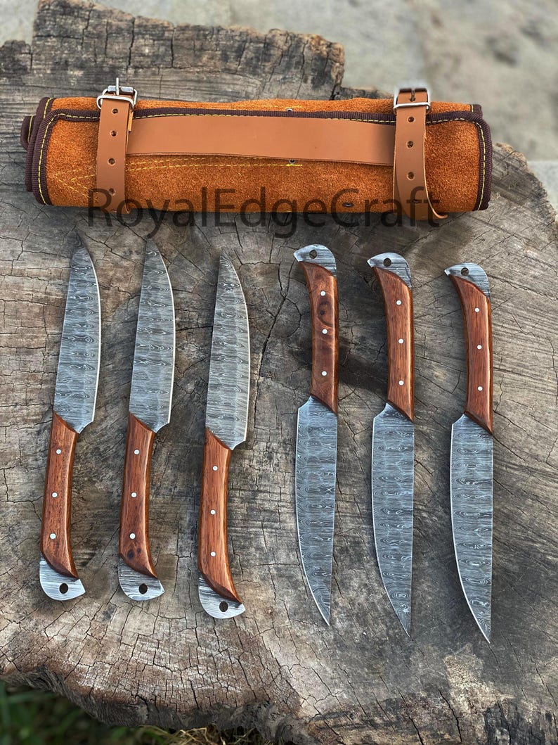 May include: A set of six Damascus steel knives with wooden handles, displayed with a brown leather knife roll. The blades have a unique patterned design. The knife roll is secured with a leather strap and buckle. The text "RoyalEdgeCraft" is visible.