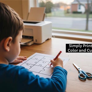 May include: A child using a red crayon to colour a jigsaw puzzle printed on white paper. Scissors with blue handles are on the table. A white printer is in the background. The text "Simply Print Color and Cut" is displayed.