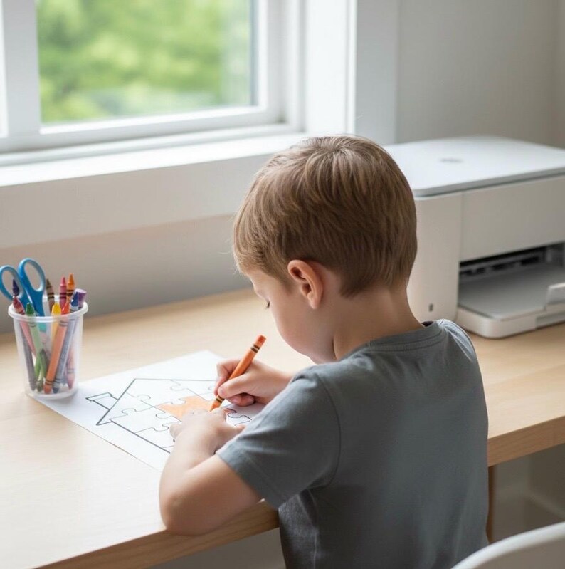 May include: A child coloring a house-shaped puzzle with an orange crayon. A clear plastic cup holds crayons and scissors. A white printer sits on the desk. The child wears a gray t-shirt.