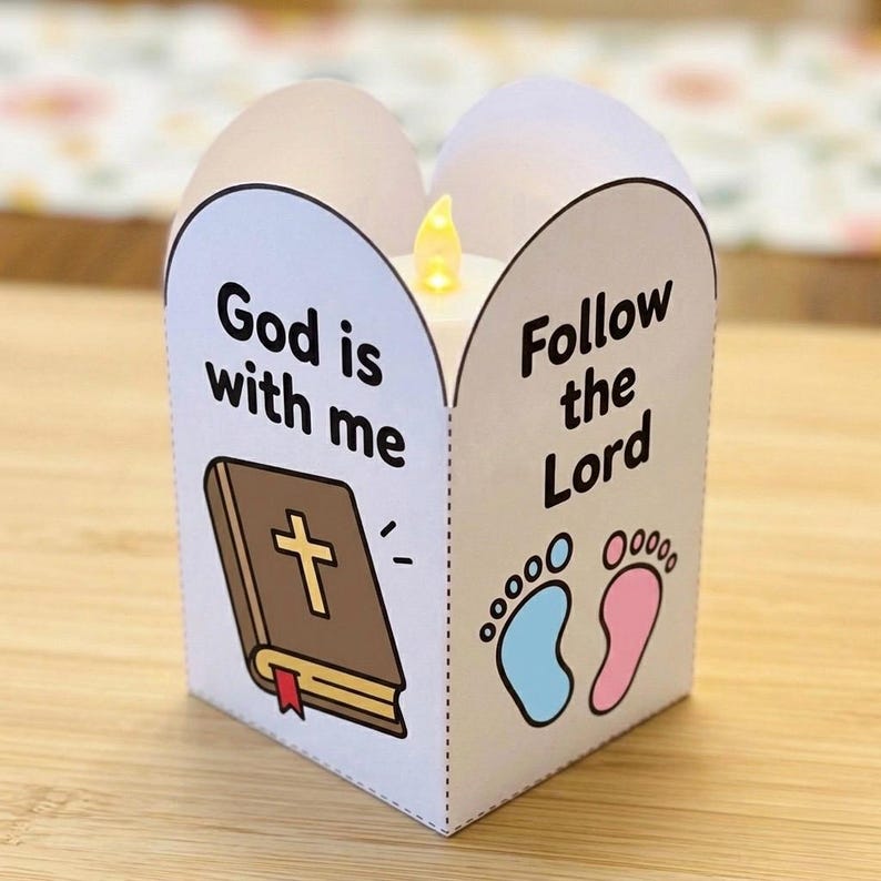 May include: A white paper lantern with a battery-operated LED candle inside. The front features a brown Bible illustration with the text God is with me and a pair of baby footprints in blue and pink with the text Follow the Lord printed on the side.
