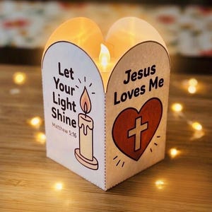 May include: A white paper lantern with a curved top edge featuring a lit LED candle inside. One side displays a candle illustration with the text Let Your Light Shine Matthew 5:16. The other side shows a red heart with a cross and Jesus Loves Me.