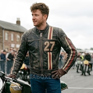 May include: A distressed brown leather motorcycle jacket with white and red stripes on the sleeves and a large "27" patch. The jacket has a quilted shoulder design and a zipper closure. The person is wearing blue jeans and brown gloves.