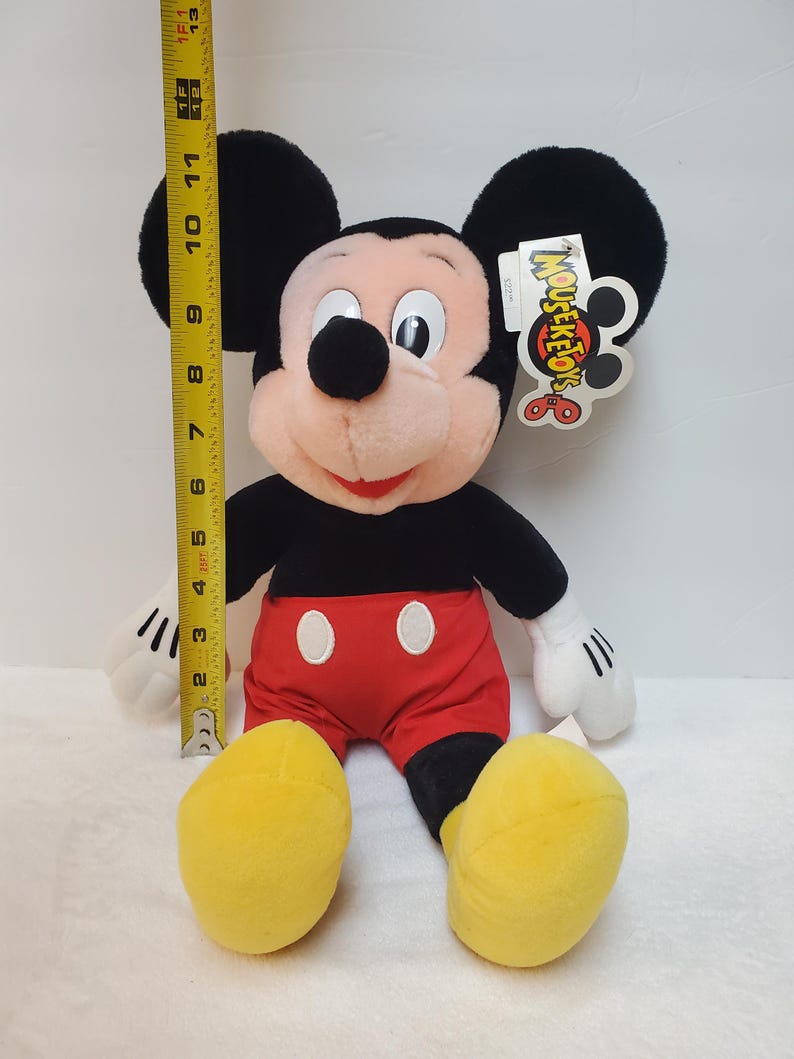 May include: A plush Mickey Mouse doll, approximately 33 cm tall, with black ears, a black body, red shorts, and yellow shoes. The doll has white gloves and a tag that reads "MOUSE-KE-TOYS".