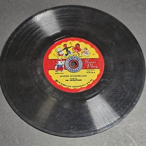 May include: A vintage black vinyl record with a red and yellow label. The label reads "Cricket Records" and "Winter Wonderland" with cartoon characters. The record is a bonus play 7CX1-A.