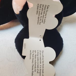 May include: A black plush toy with a tag that reads "This soft toy has been made of all new materials, it is designed to bring smiles to kids of all ages. Made exclusively for The Walt Disney Theme Parks and Resorts."
