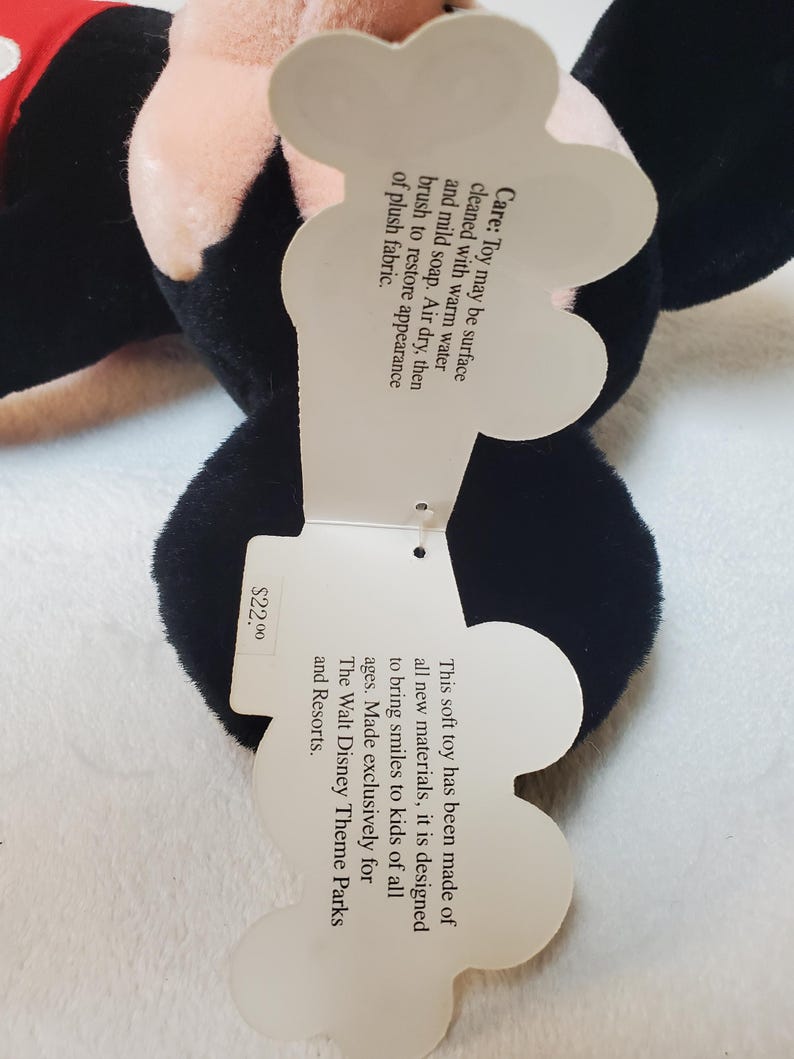 May include: A black plush toy with a tag that reads "This soft toy has been made of all new materials, it is designed to bring smiles to kids of all ages. Made exclusively for The Walt Disney Theme Parks and Resorts."