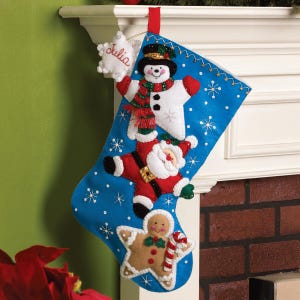 May include: A blue Christmas stocking featuring a snowman, Santa Claus, and gingerbread man. The stocking is decorated with white snowflakes and a red hanging ribbon. A white star with the name "Julia" is attached.