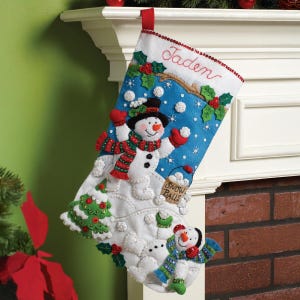 May include: A festive Christmas stocking featuring a snowman design. The stocking is predominantly white and blue, with a red trim and the name "Jaden" embroidered. The snowman wears a black hat, red scarf, and mittens. Includes holly and snowballs.