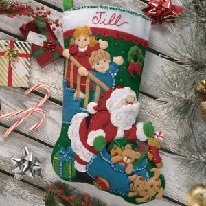 Könnte beinhalten: Handgefertigter Weihnachtsstrumpf mit einem Filz-Weihnachtsmann-Design, Kindern und dem Namen "Jill" auf der Oberseite gestickt. Der Strumpf ist mit Pailletten verziert und enthält ein kleines Geschenk und einen Hund.