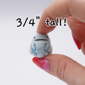 May include: A small, light blue plush figure, approximately 0.75 inches tall, with embroidered details. The figure is held between fingers against a white background. The text "3/4" tall!" is written above the figure.