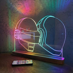 May include: A neon-style LED lamp with a helmet design, set on a wooden base, and a remote control. The lamp emits a colourful glow, with the helmet outline lit in various hues. The remote control has multiple buttons.