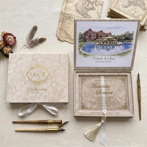 May include: A beige velvet-textured box with gold foil lettering V&O and The Wedding, containing a clear acrylic invitation with gold text for Matumba and Someni. The lid interior features a watercolor of a resort, accompanied by three calligraphy pens.
