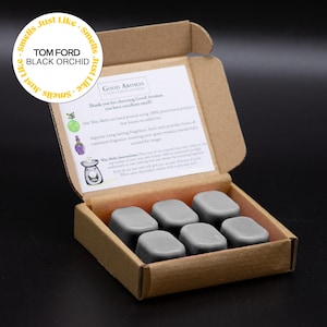 May include: A box of six grey wax melts, with a printed card and a circular sticker that reads "TOM FORD BLACK ORCHID." The wax melts are rectangular and the box is made of cardboard.