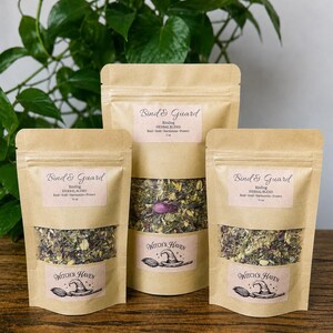 K&ouml;nnte beinhalten: Drei braune Papiert&uuml;ten mit Kr&auml;utermischung, beschriftet mit "Bind & Guard" und "Witch's Haven". Die Beutel enthalten getrocknete Kr&auml;uter und eine Grafik mit Hexenhut und Besen. Im Hintergrund ist gr&uuml;nes Laub zu sehen.