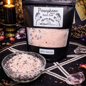 May include: A black bag of Persephone Bath Salt, 2.05 ounces, with a clear bowl of bath salt in front. The bag has a label with two women, a witch's hat, and the words "Witch's Haven". The text "Ritual Herbal Soak" is below the bowl.