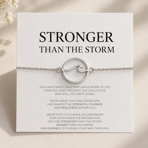 May include: A silver-toned chain bracelet featuring a circular charm with a wave cutout design. The bracelet is attached to a white display card printed with the text STRONGER THAN THE STORM and a message about resilience and inner strength.