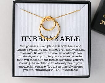 May include: A gold-colored necklace with two interlocking circles, presented in a black box with the word "UNBREAKABLE" and inspirational text. The box also has the text "Stay strong believe in yourself & chase your dreams."