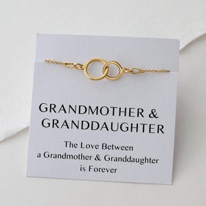 May include: A gold-colored bracelet with two interlocking circles, displayed on a white card. The card reads "GRANDMOTHER & GRANDDAUGHTER" with the text "The Love Between a Grandmother & Granddaughter is Forever."