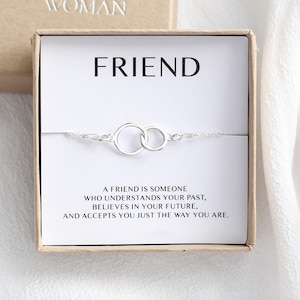 May include: A silver friendship bracelet with two interlocking circles, displayed in a gift box. The box features the word "FRIEND" and a quote about friendship.
