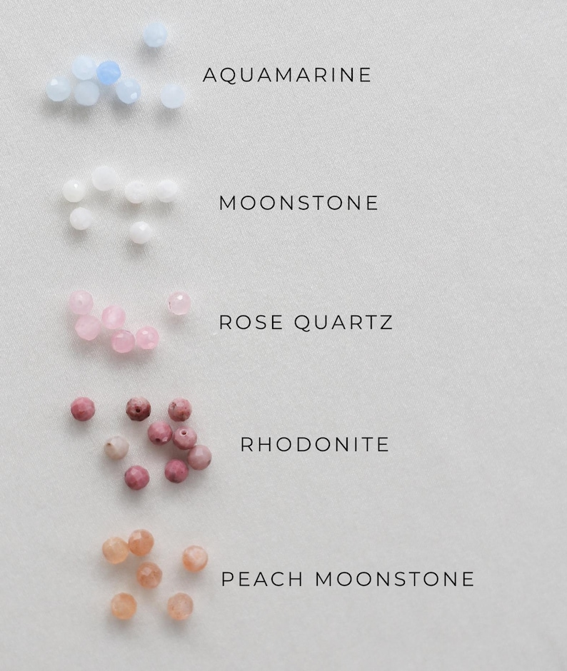 May include: An overhead shot displays five types of gemstone beads: aquamarine, moonstone, rose quartz, rhodonite, and peach moonstone. Each gemstone is accompanied by its name in a clean, sans-serif font. The beads are small and round, with varying shades of blue, white, pink, and peach.