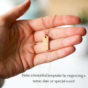 Puede incluir: Un collar con colgante rectangular de tono dorado que presenta la letra A grabada, un peque&ntilde;o s&iacute;mbolo de coraz&oacute;n y la letra J. El colgante cuelga de una delicada cadena dorada. El texto inferior dice: Make a beautiful keepsake by engraving a name, date, or special word.