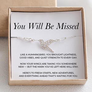 May include: A silver hummingbird bracelet presented in a gift box. The box includes a card with the text "You Will Be Missed" and a message about new beginnings. The bracelet has a delicate, openwork design.