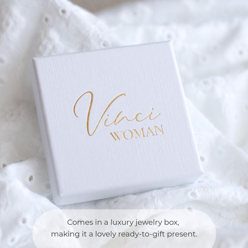 May include: A white square jewelry box with the gold text "Vinci WOMAN" on the top. The box is on a white, textured surface. The text "Comes in a luxury jewelry box, making it a lovely ready-to-gift present" is at the bottom.