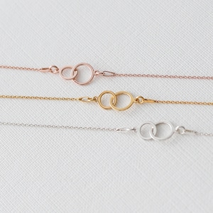 Puede incluir: Tres delicadas pulseras de cadena en oro rosa, oro y plata. Cada pulsera presenta dos c&iacute;rculos entrelazados como elemento central. Las pulseras se muestran sobre una superficie blanca, mostrando su estilo minimalista.