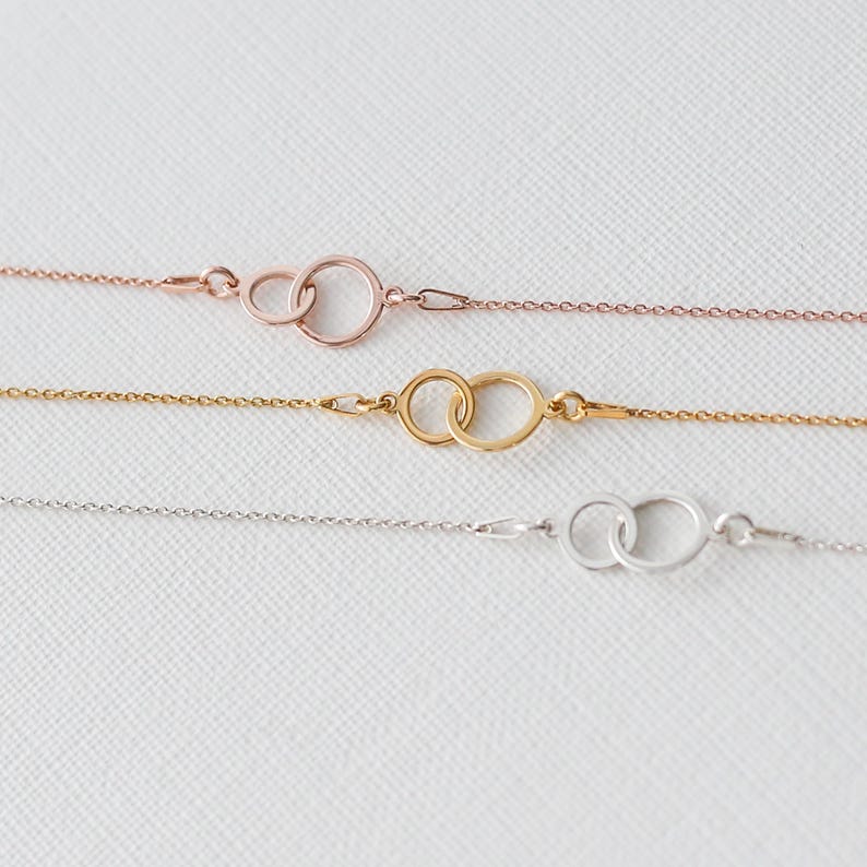 Puede incluir: Tres delicadas pulseras de cadena en oro rosa, oro y plata. Cada pulsera presenta dos c&iacute;rculos entrelazados como elemento central. Las pulseras se muestran sobre una superficie blanca, mostrando su estilo minimalista.