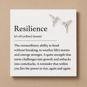 Könnte beinhalten: Eine weiße quadratische Karte mit der Definition des Wortes Resilience, phonetischer Schreibweise und einem Textabsatz. Zwei kleine silberne Ohrstecker in Form von Kolibris sind in der oberen rechten Ecke der Karte befestigt.